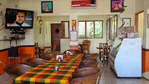 A restaurant with a long communal table, multiple chairs, a television, and a refrigerator. - Hotel San Cristobal (Guasave)