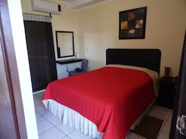 Un dormitorio con cama, escritorio, silla, espejo e imagen en la pared.