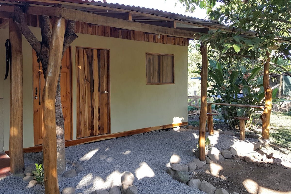 A rustic building with wooden doors and a small window, surrounded by gravel and rocks.