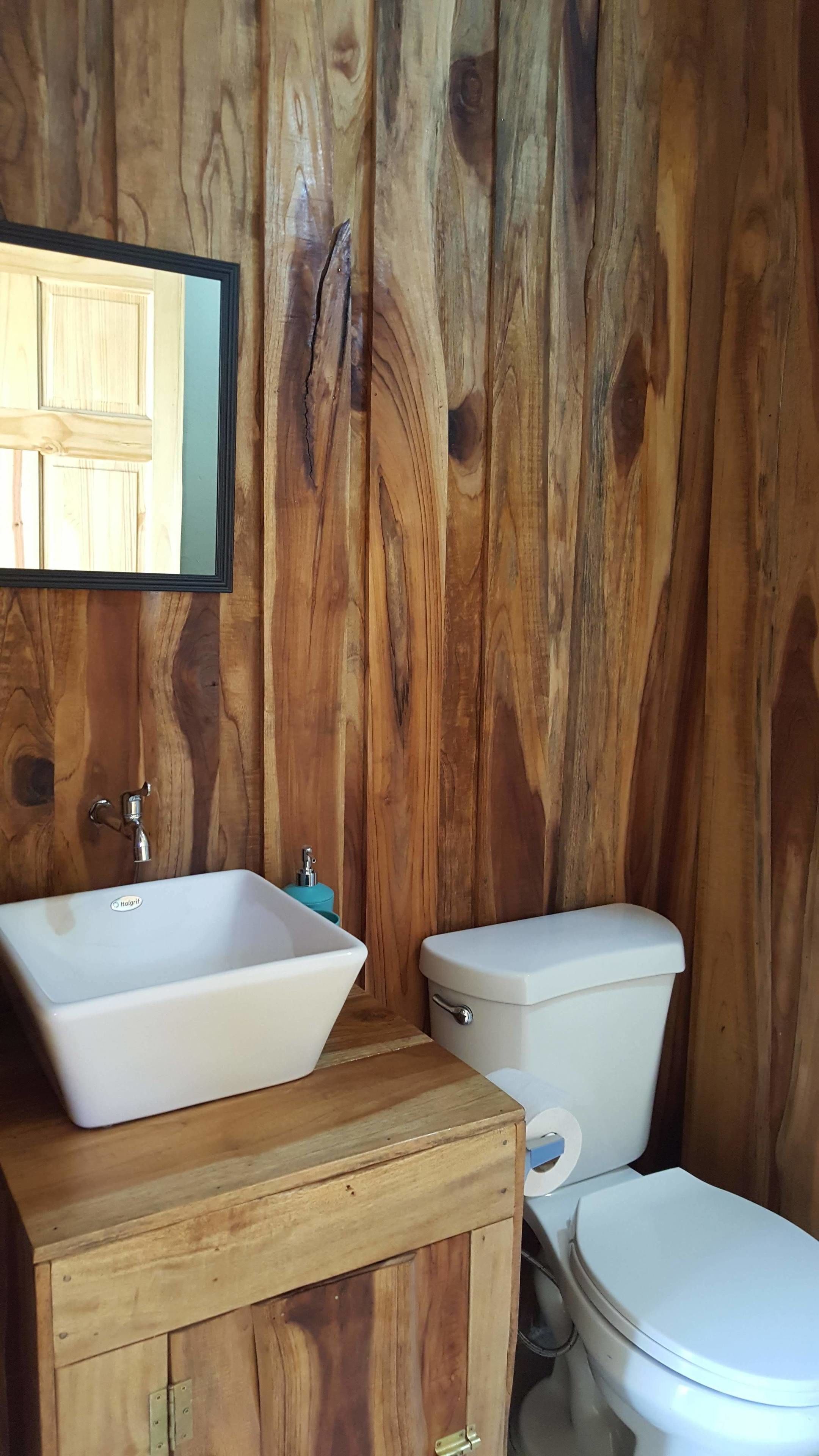 Un baño con pared de madera, lavamanos blanco y un inodoro.