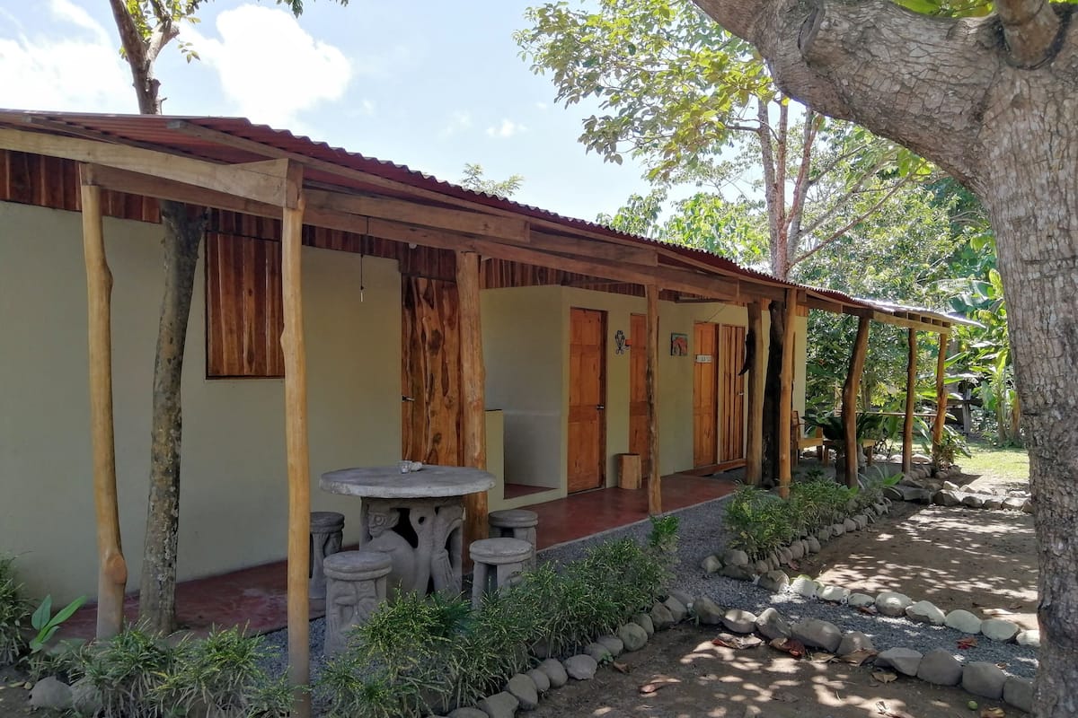 A rustic wooden building with a covered porch, stone seating, and a small table.