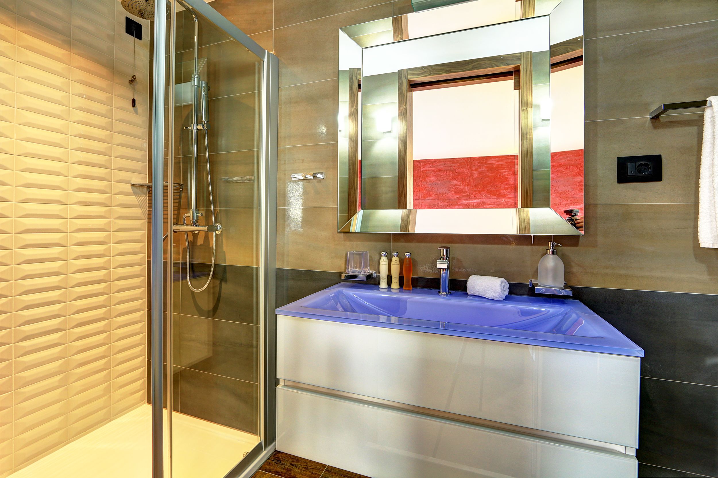 A modern bathroom with a glass shower enclosure, a blue sink, and a large mirror.