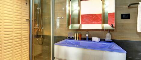 A modern bathroom with a glass shower enclosure, a blue sink, and a large mirror.