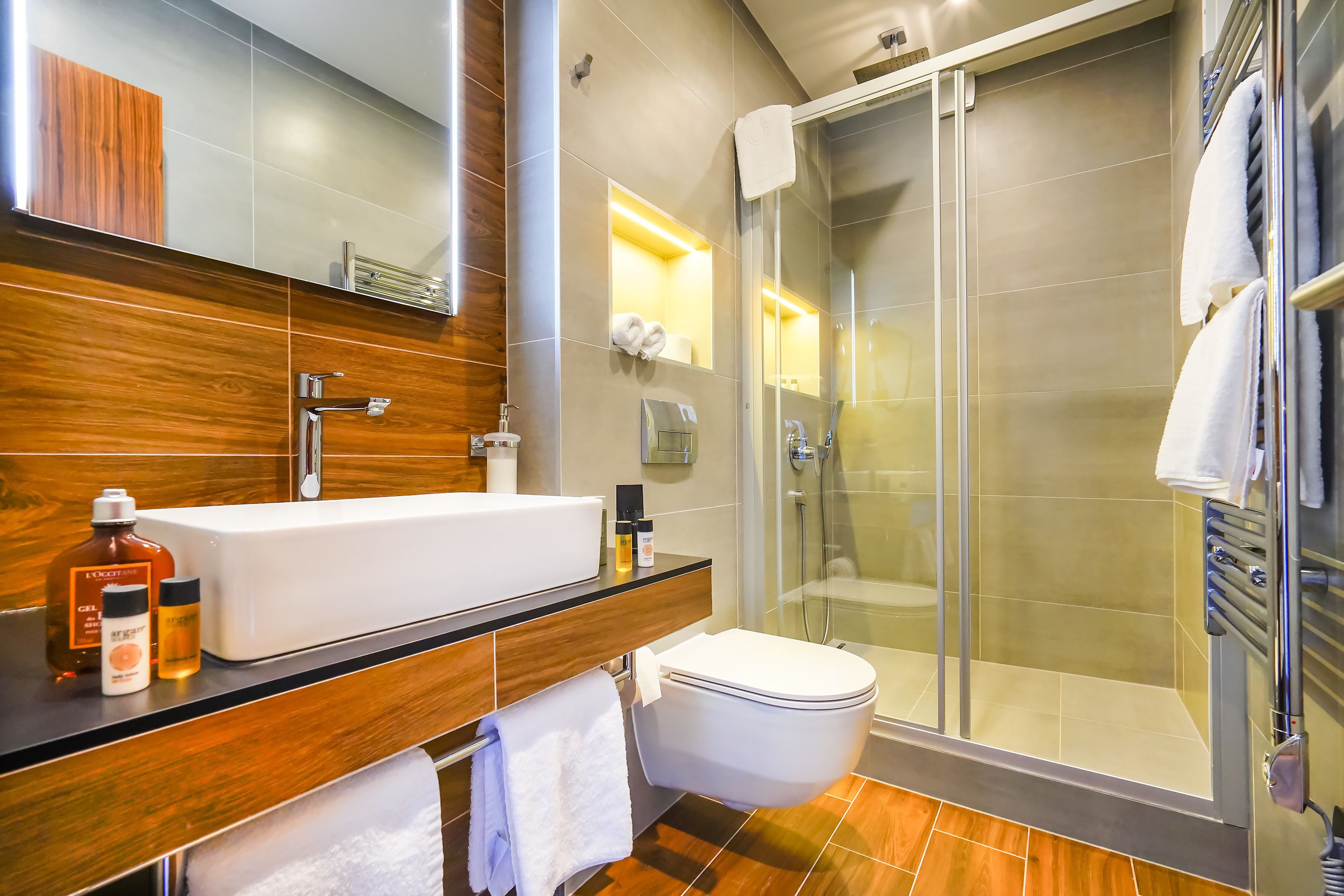 A modern bathroom with a wooden vanity, a white sink, and a glass-enclosed shower.