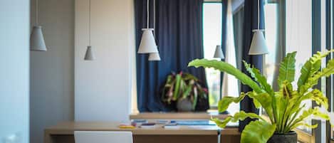 A modern room with a laptop on a wooden desk, a potted plant, and a window with curtains.