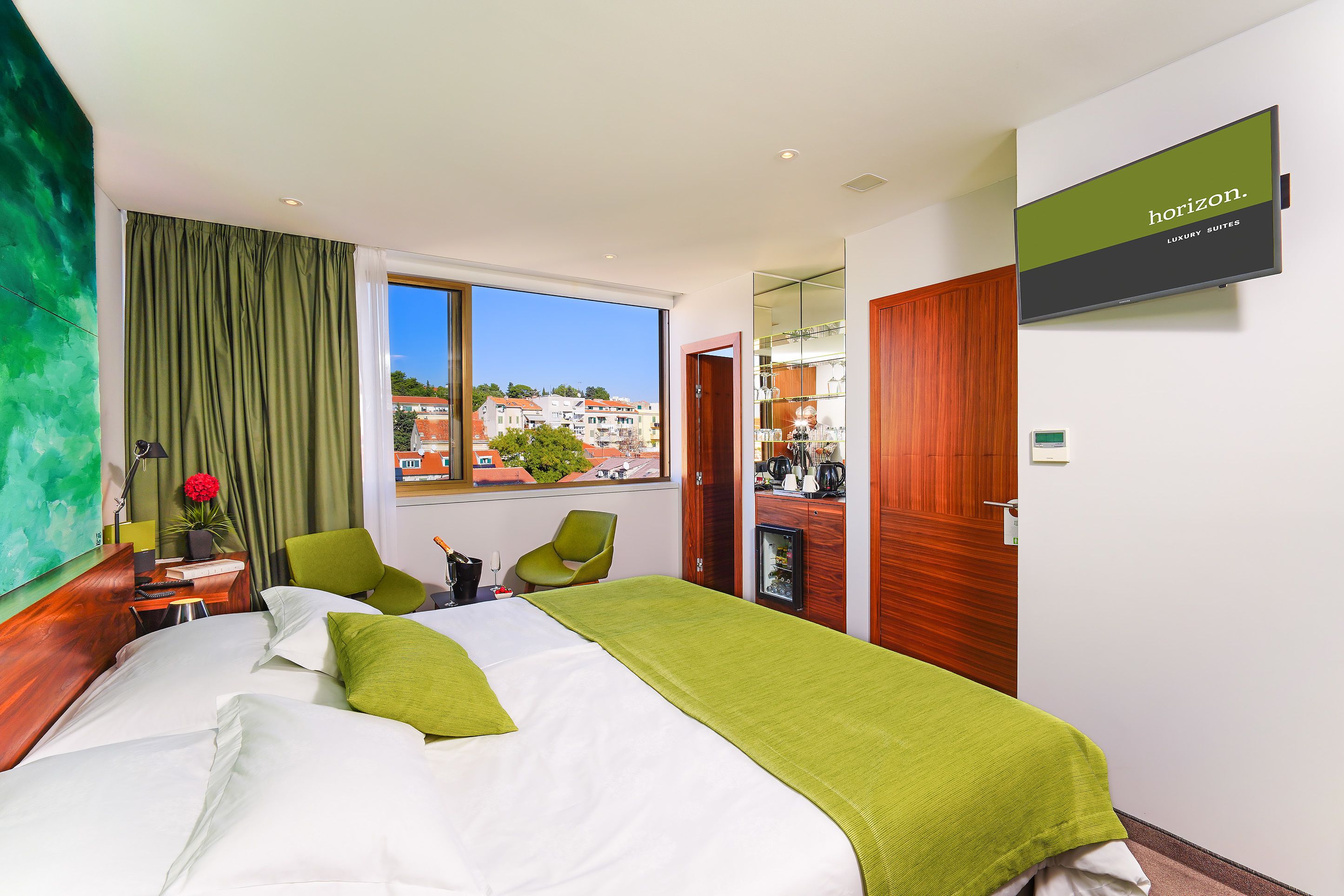 Une chambre d’hôtel avec un lit, un bureau, une chaise, une télévision et une vue sur la ville.