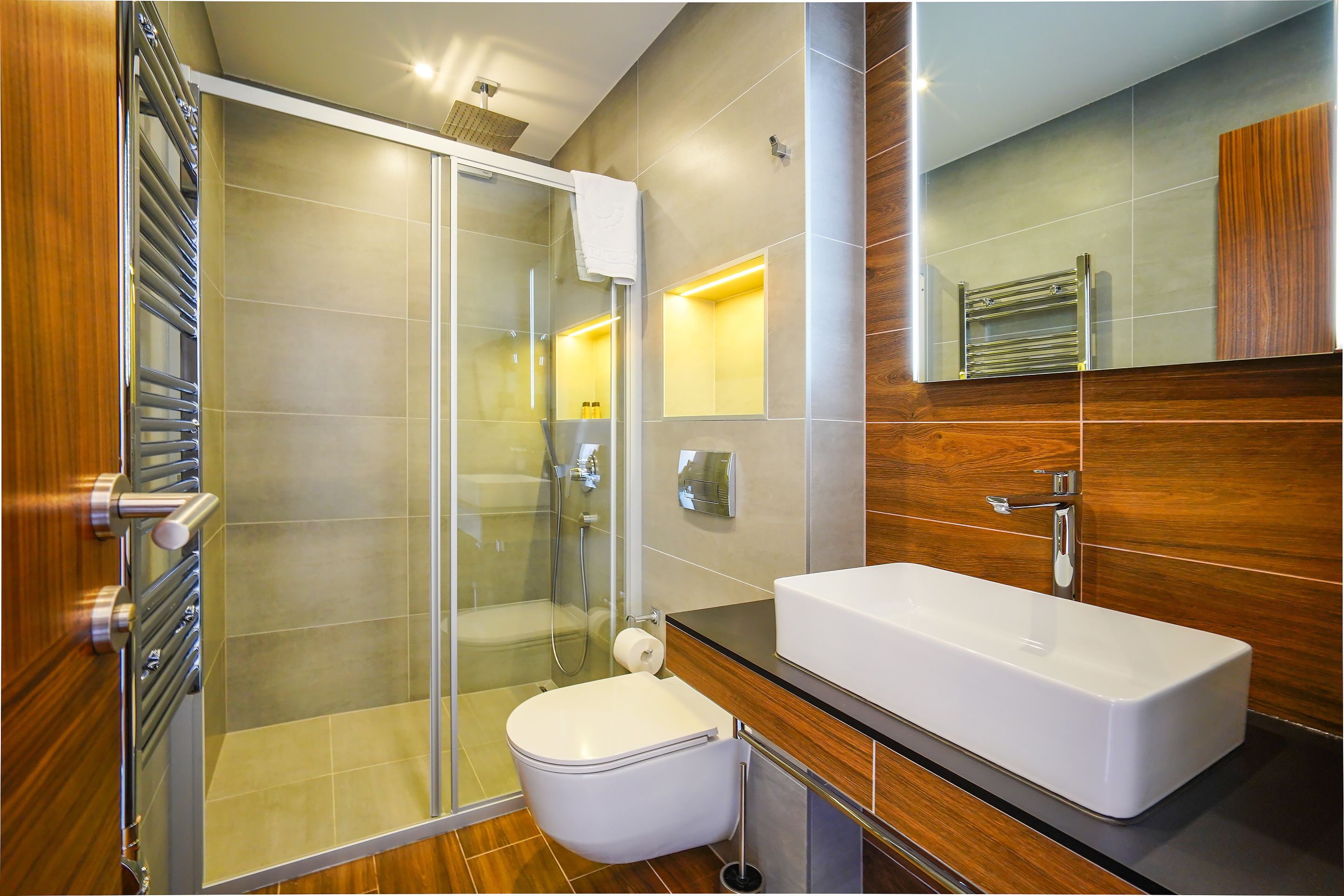 A modern bathroom with a glass shower enclosure, a white sink, and a wooden vanity.
