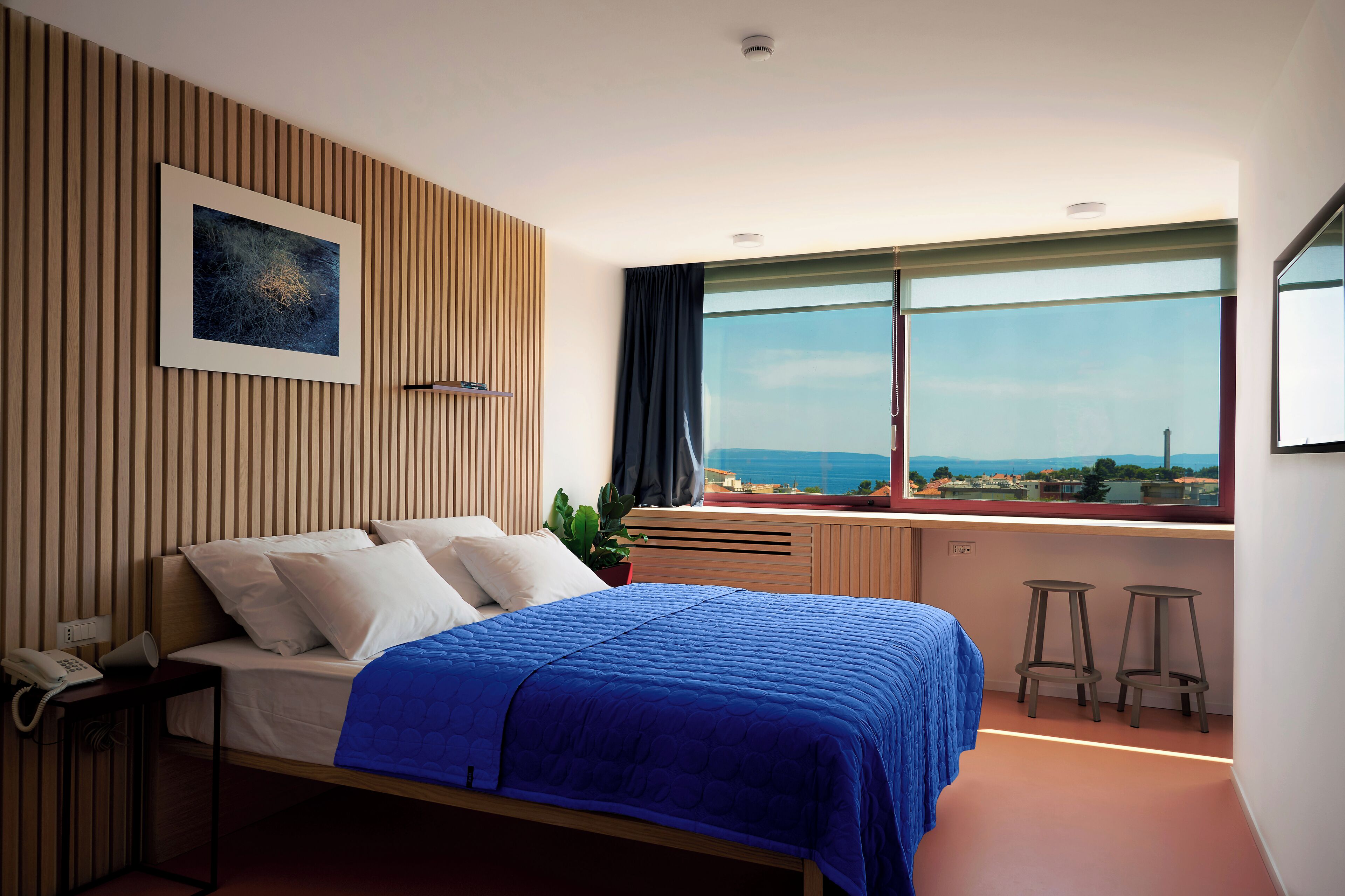 A modern bedroom with a bed, a nightstand, a telephone, a window with a view, and a plant.