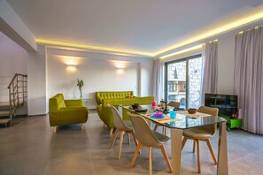 A modern living room with a glass dining table, green sofa, and a TV.