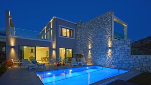 Una casa moderna amb piscina, mur de pedra i zona d'estar a l'aire lliure.