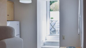 A compact kitchen with a dining area, a refrigerator, a hanging light fixture, and a view through an open door to an outdoor area. - Apartment in Ag.Anna area,fully equipped,semi-basement & very quiet environment. (Νάξος)