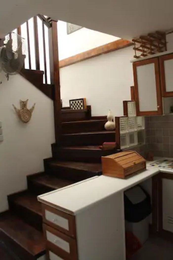 Una cucina con scale in legno, un piano di lavoro bianco e un piccolo cestino.