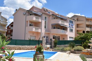 A multi-story hotel with balconies, a swimming pool, and a garden area.