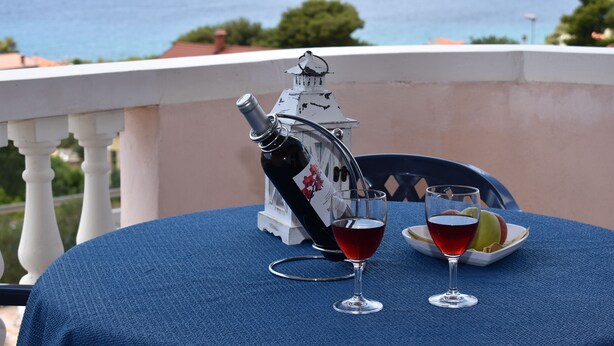Ein Tisch mit einer Weinflasche und zwei Weingläsern, ein Teller mit Früchten und im Hintergrund eine malerische Aussicht auf Meer und Berge.