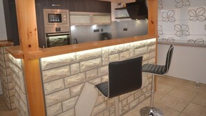 Eine Küche mit Steinrückwand, Holztischplatte und zwei schwarzen Barhocker.