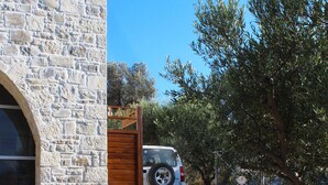 A stone building with a gravel driveway and a parked SUV. - Villa Marikami, an amazing new stone built house in Kamilari (Καμηλάρι)