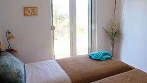 A bedroom with a bed, a window, a vase with dried plants, and a wall-mounted picture. - Villa Marikami, an amazing new stone built house in Kamilari (Καμηλάρι)