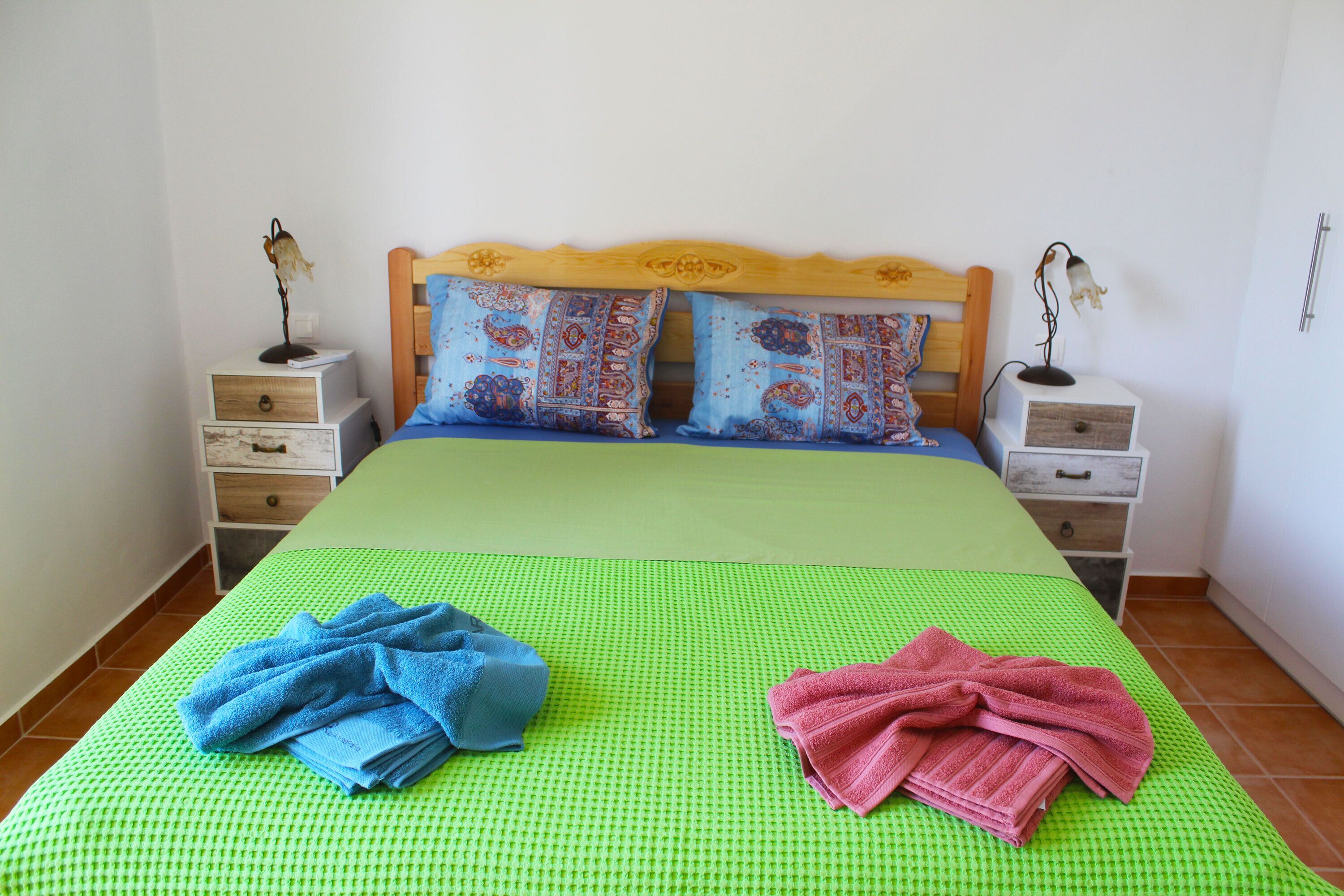 Una cama con una colcha verde a cuadros, dos almohadas con estampados de estilo paisly y dos mesitas de noche con lámparas y cajones.