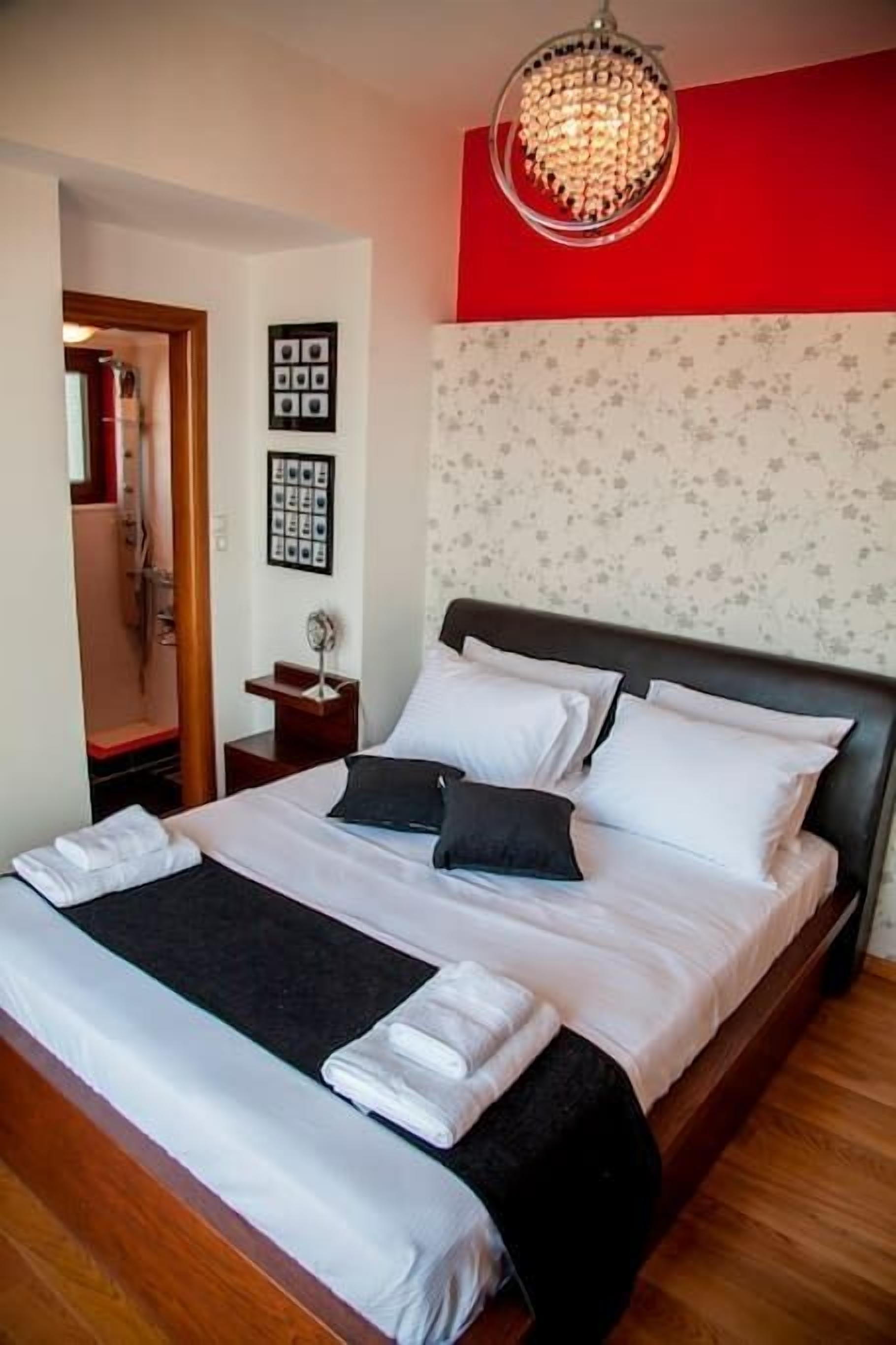 A neatly made bed with white and black bedding, a wooden headboard, and a chandelier above.