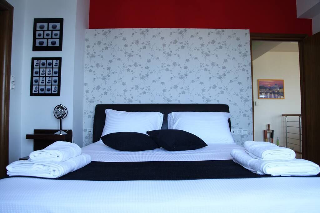 A neatly made bed with white and black bedding, a floral wallpaper headboard, and a red accent wall.