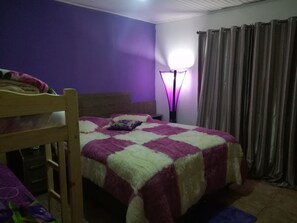 A bedroom with a bed, a nightstand, a lamp, and a window with curtains.