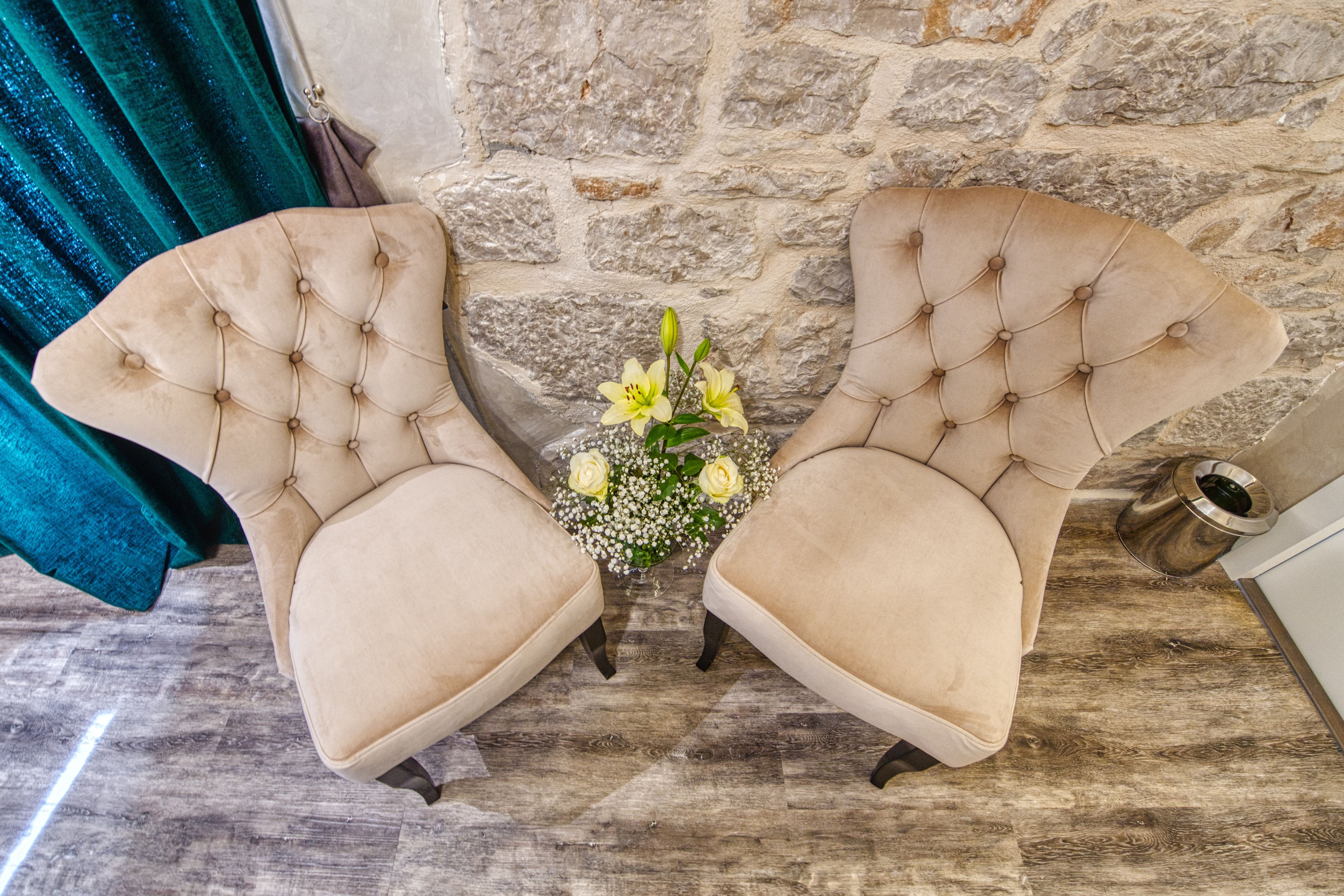 Two tufted armchairs facing each other with a small table and flowers between them, set against a stone wall and wooden floor.