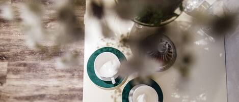 Una mesa con dos tazas blancas sobre platillos verdes, un vaso de agua y un fondo desenfocado.