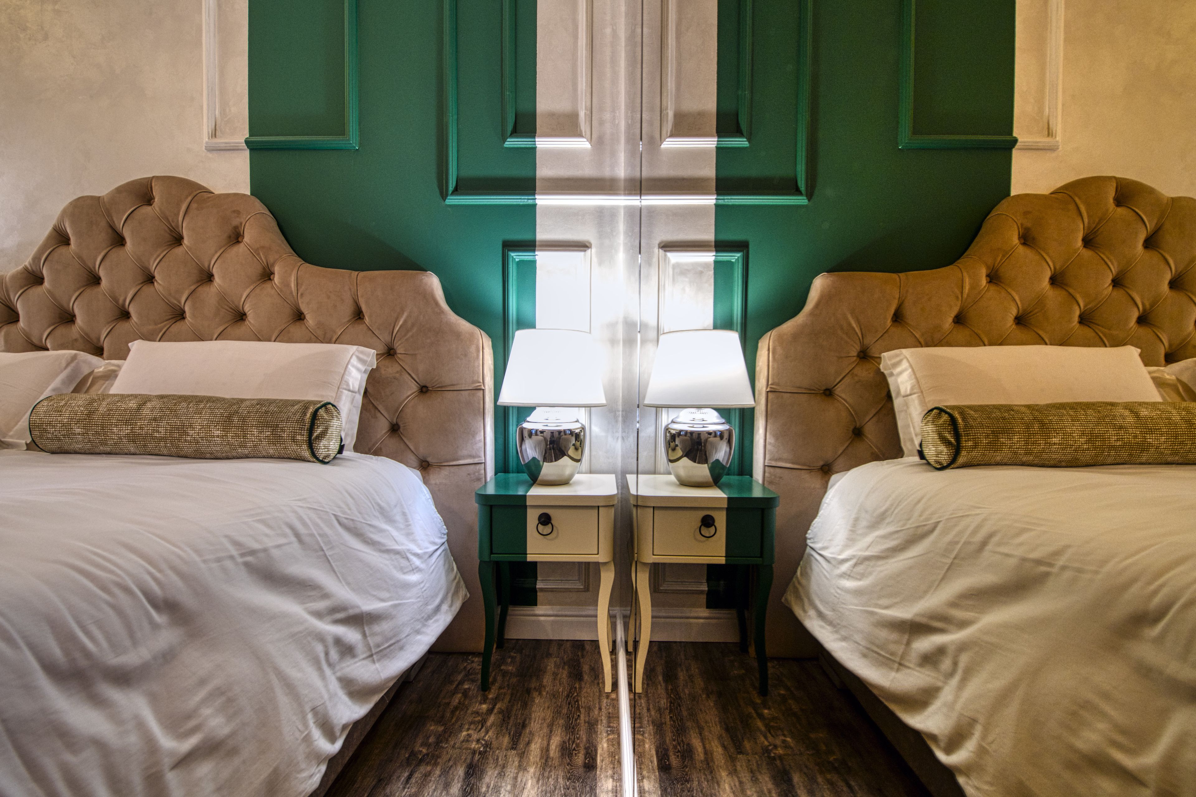 A hotel room with two beds, each with a tufted headboard, a nightstand with a lamp, and a mirror.