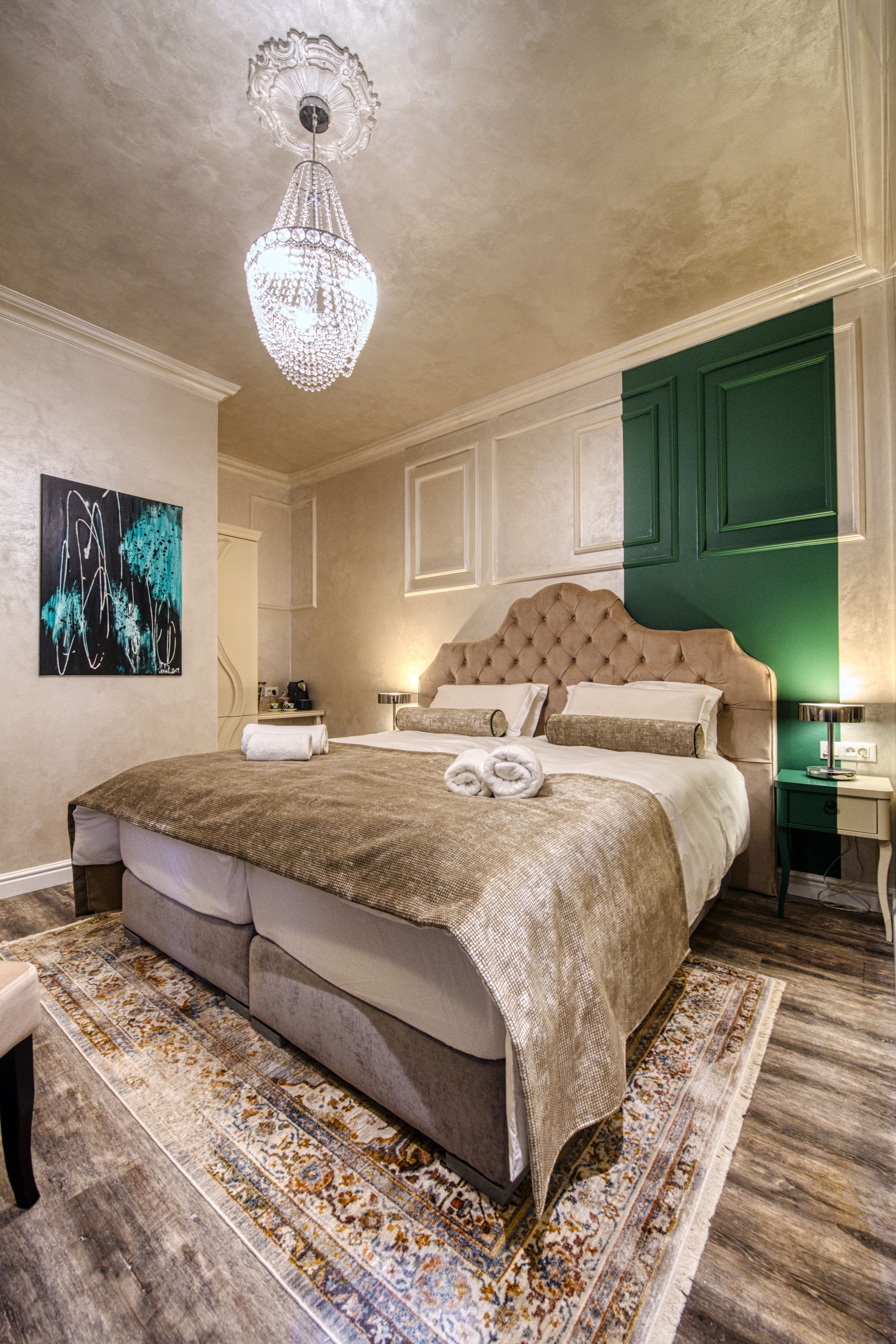 Een ruime slaapkamer met een groot bed, een kroonluchter, een groene deur en een schilderij aan de muur.