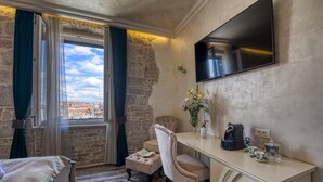 A hotel room with a bed, a desk with a coffee maker, a vase with flowers, and a TV on the wall. - Riva Palace - design rooms (Zadar)