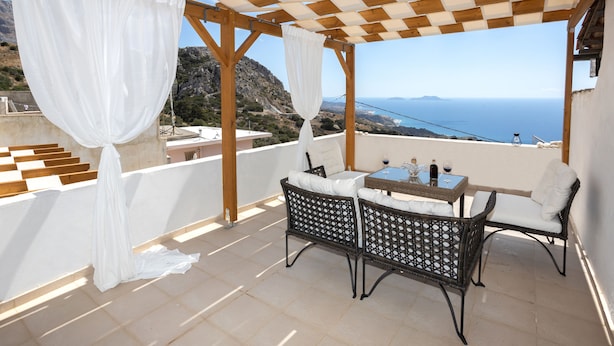 Un espace extérieur aménagé, abrité et doté de mobilier en osier et d’une table, offrant une vue panoramique sur un paysage côtier pittoresque.