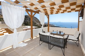 A covered outdoor seating area with wicker furniture and a table, overlooking a scenic coastal landscape.