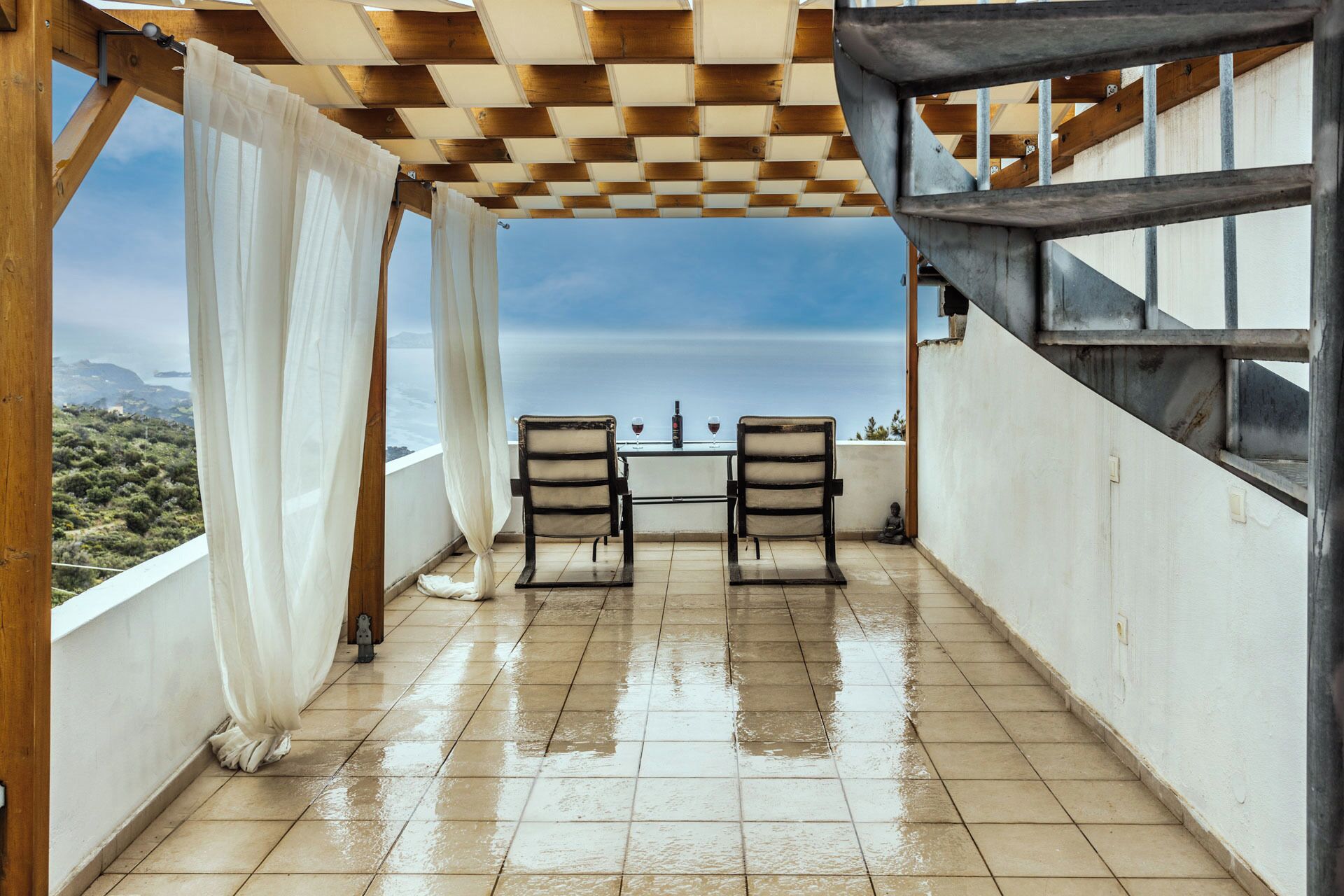 Un espace extérieur abrité, doté d’un plafond à carreaux, de deux chaises et d’une table avec des verres.