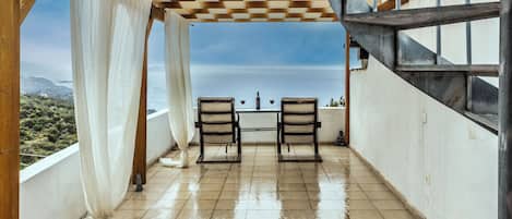 Un espacio al aire libre cubierto con techo a cuadros, dos sillas y una mesa con vasos.