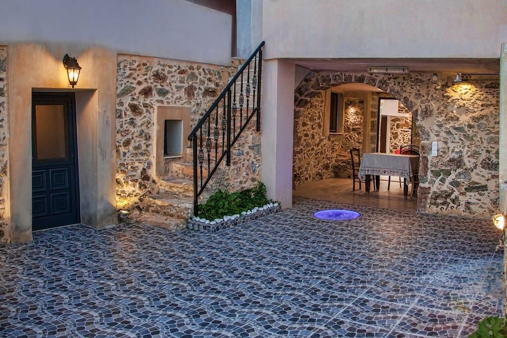 Une cour aux murs de pierre, dotée d’un sol carrelé, d’un escalier et d’un coin repas avec une table et des chaises.