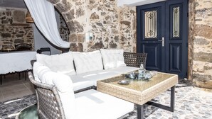 Une pièce avec un mur en pierre, un canapé blanc, une table basse en osier et une porte bleu foncé.