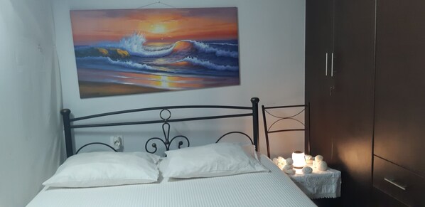 A bedroom with a bed, a painting of a sunset over the ocean, and a bedside table with candles.