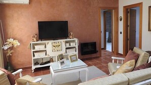 Una sala de estar con televisión de pantalla plana, muebles blancos, chimenea y una puerta que da a otra habitación.