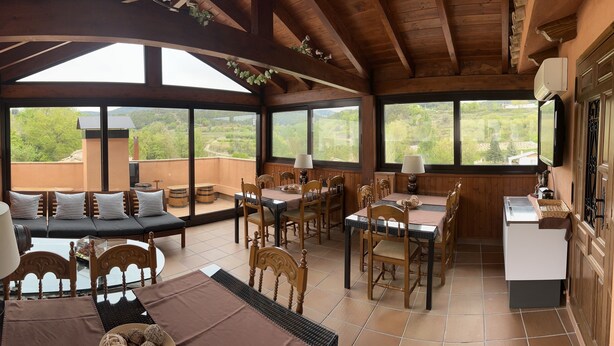 Un comedor amplio con mobiliario de madera, ventanas grandes que ofrecen vistas panorámicas y una zona de estar acogedora con cojines.