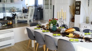 En matplats med ett bord dukat för sex personer, med en vit duk, grå stolar och en central ljusstake med ljus.
