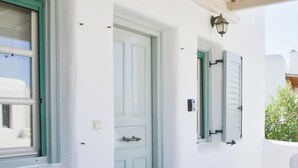 Un patio con una mesa de madera, dos plantas blancas en macetas y una puerta azul.