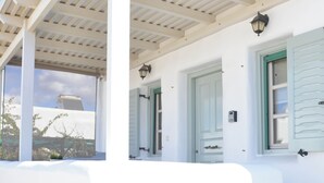 Un edificio blanco con un porche cubierto, una puerta y una ventana con contraventanas.