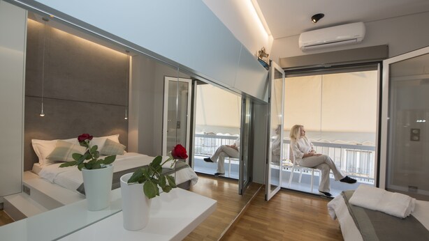 Una habitación de hotel moderna con cama, zona de estar, balcón con barandilla y un espejo grande.