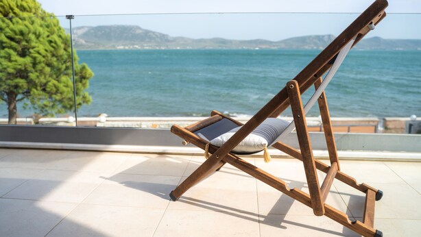 A wooden lounge chair with a cushion on a tiled balcony overlooking a body of water and distant hills. - A Family Friendly Sea View Villa. Cycling Walking Fishing Birdwatcing Swimming (Πηγαδάκια)