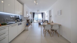 A modern kitchen with white cabinets, a dining area with a table and chairs, and a view of the outdoors through a large window.