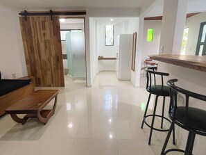 A modern kitchen with a wooden bar counter and stools, a sliding door, and a view into another room.