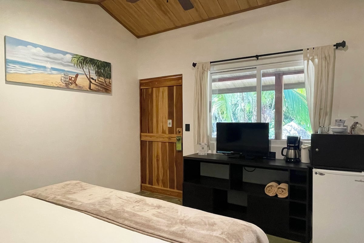 Un dormitorio con cama, televisión, cafetera y refrigerador pequeño.