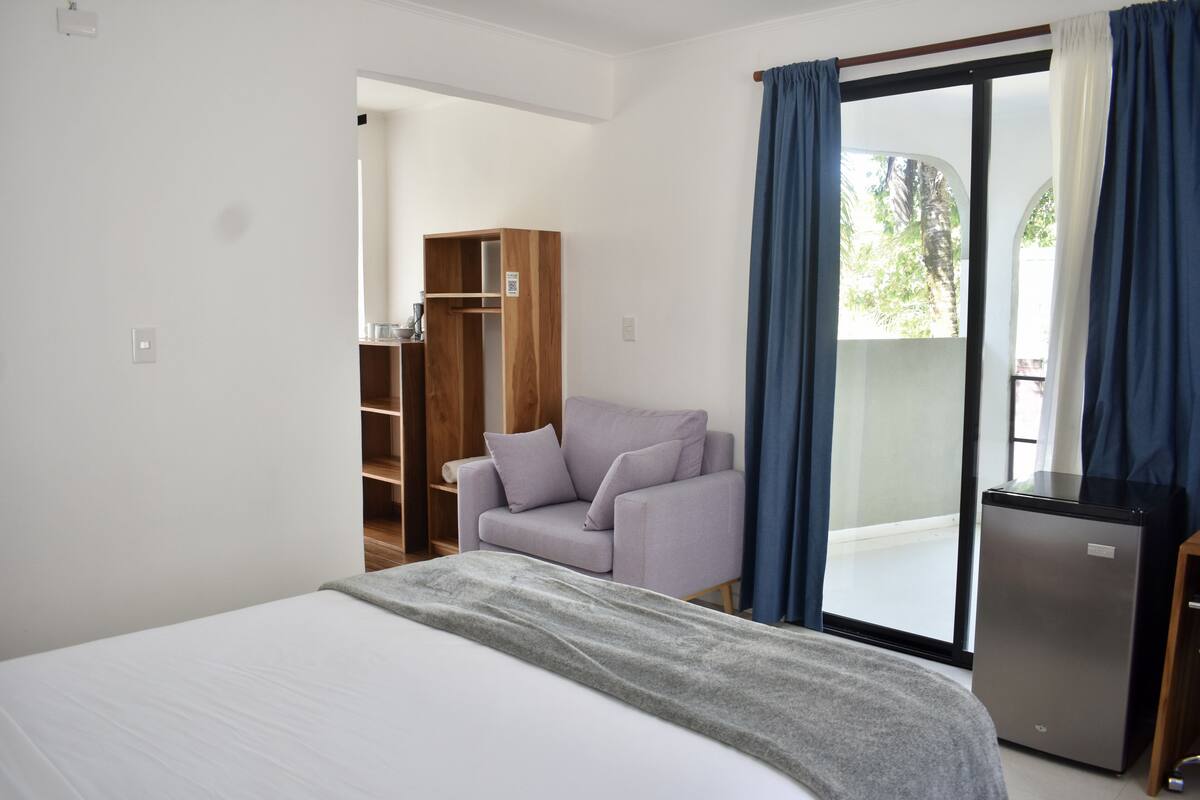 Un dormitorio con cama, armario, zona de estar y balcón con cortinas.