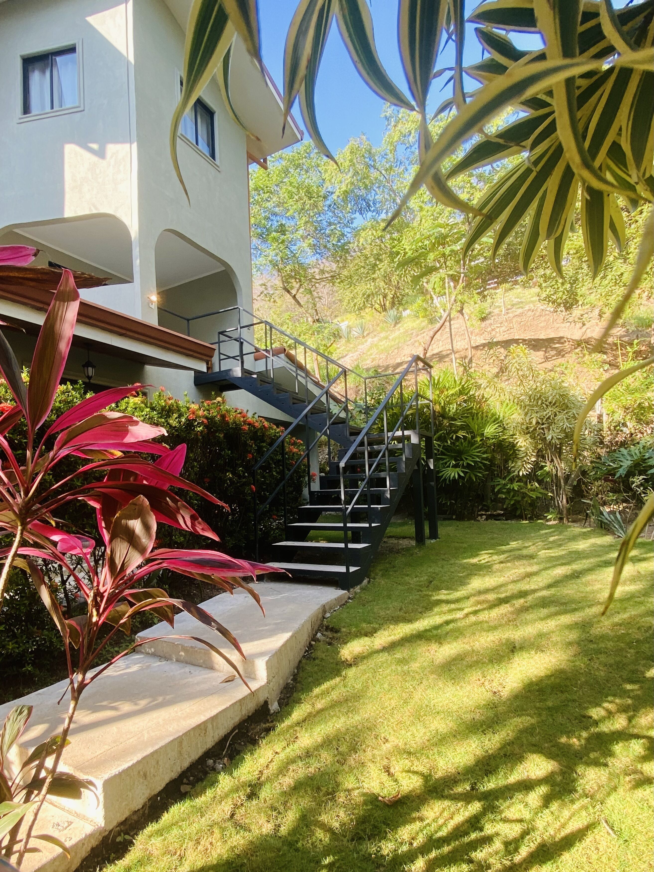 Un bâtiment moderne doté d’un escalier menant à un balcon, entouré d’une végétation luxuriante et d’une pelouse bien entretenue.