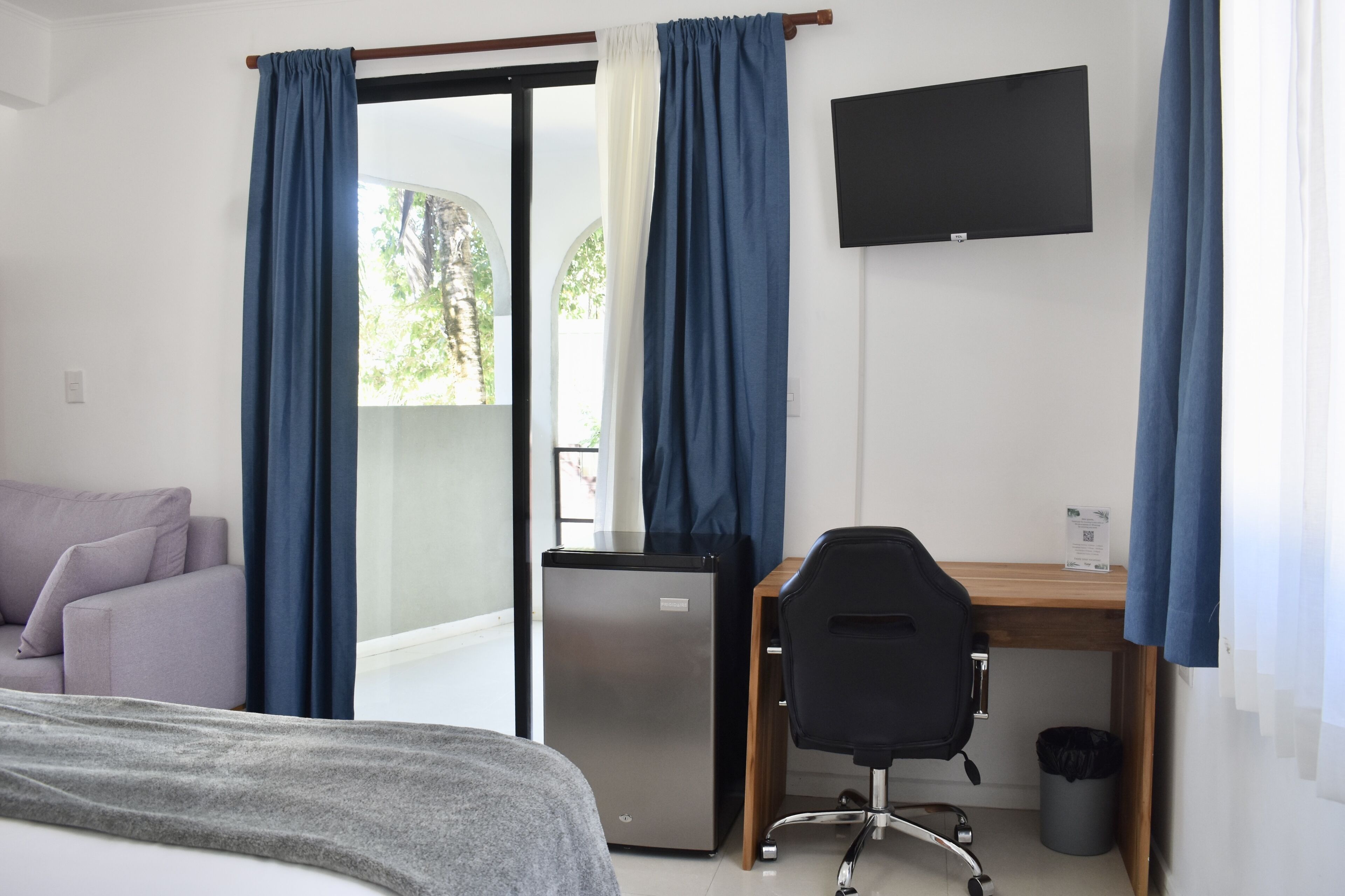 A hotel room with a bed, a desk, a chair, a refrigerator, and a TV.